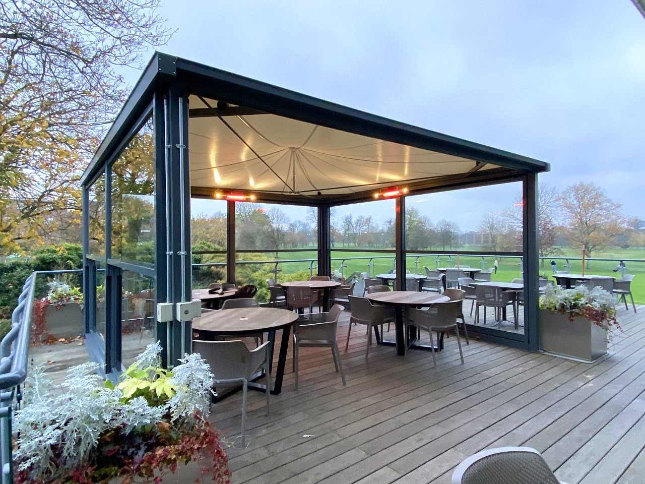 A heated canopy providing shelter for a golf club's outdoor dining area on a rainy day