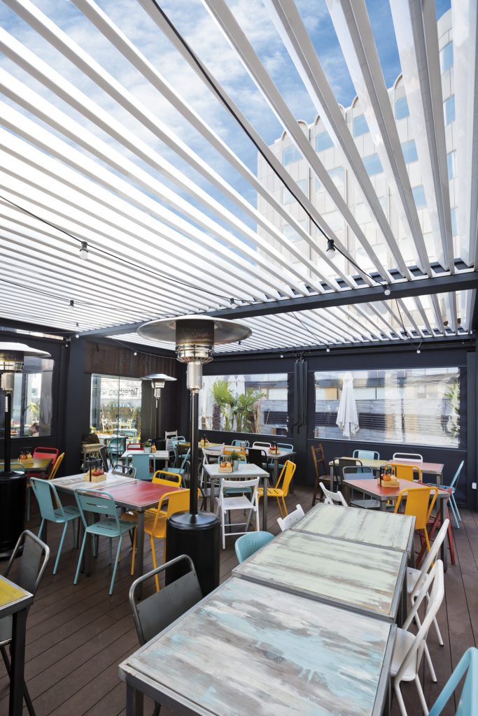 A bioclimatic pergola with motorised slats open and zip blinds lowered at a restaurant.