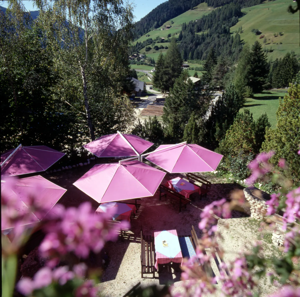 Five pink MAY Rialto Cantilever Parasols in a restaurant garden overlooking green hills.