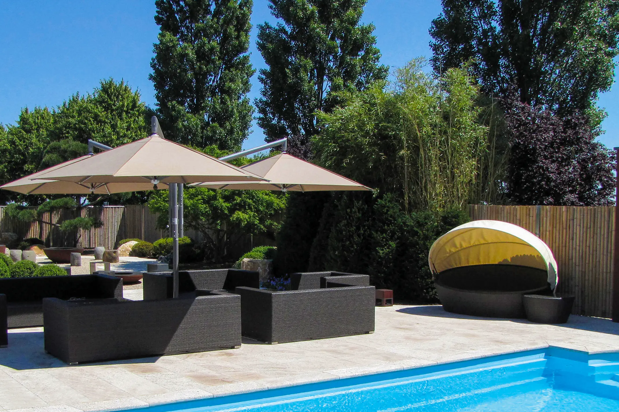 The MAY Rialto Cantilever Parasol in a summer garden with a swimming pool.