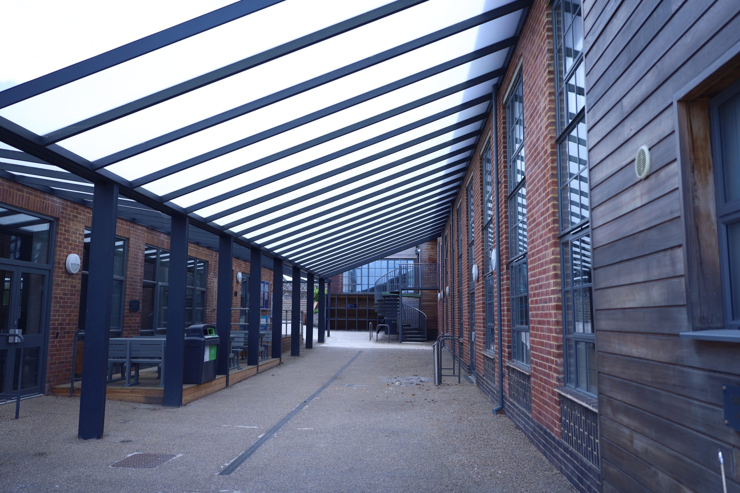 Asymmetric V-shaped Lean-to canopy sheltering a walkway between two school buildings at Seaford College 